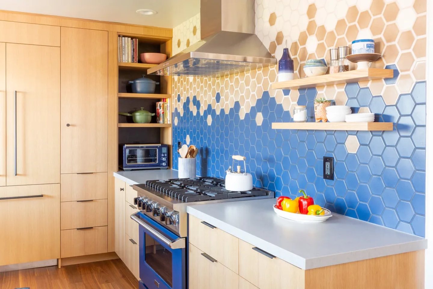 Blue hex tile backsplash behind open wood shelving in a bright kitchen