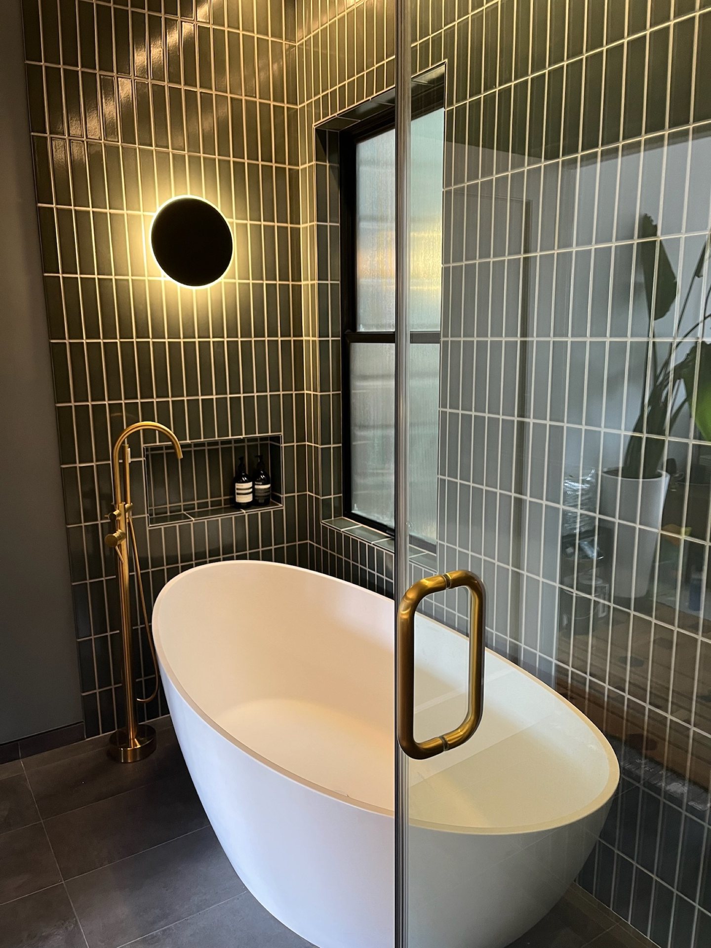 Green tile bathroom with a soaking tub and warm brass details