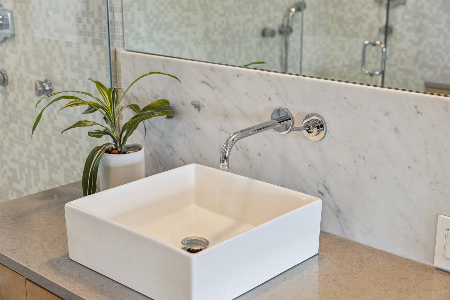 Dark stone vessel sink on a light stone vanity with warm wood cabinetry