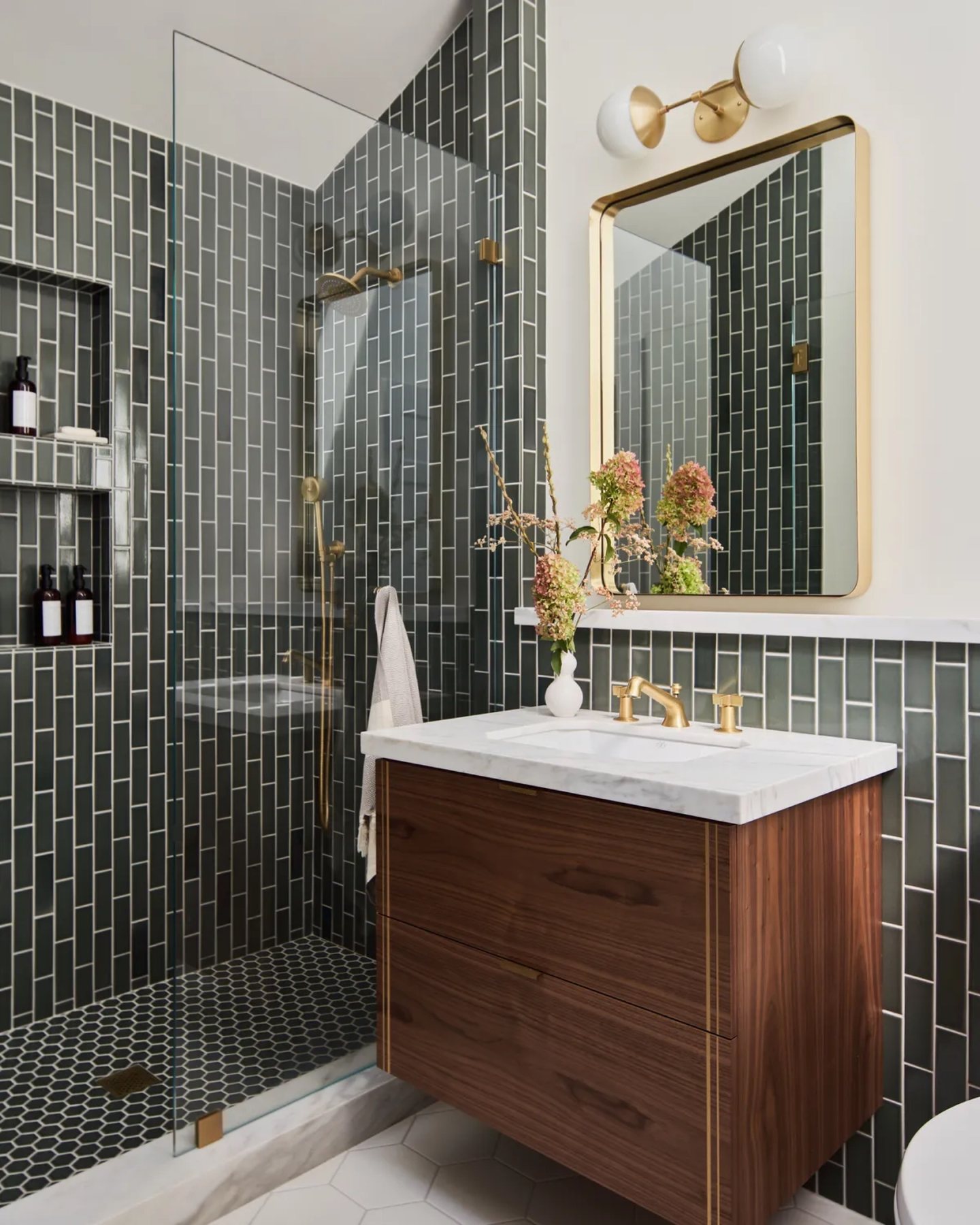 Dark green tile bathroom with a wood vanity, brass fixtures, and patterned floor